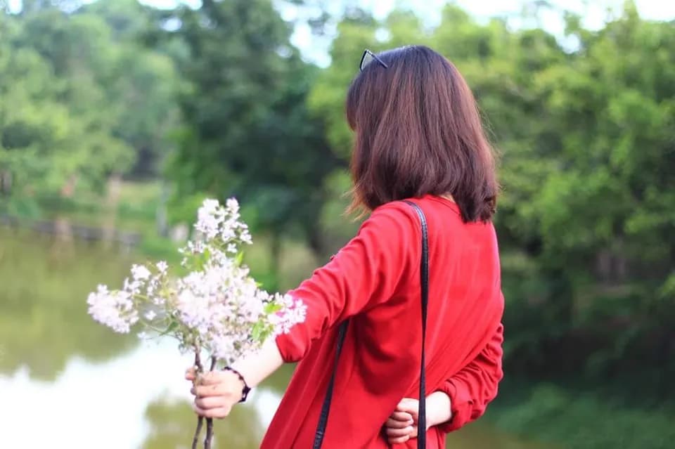 Cô gái áo đỏ cầm bó hoa bên hồ