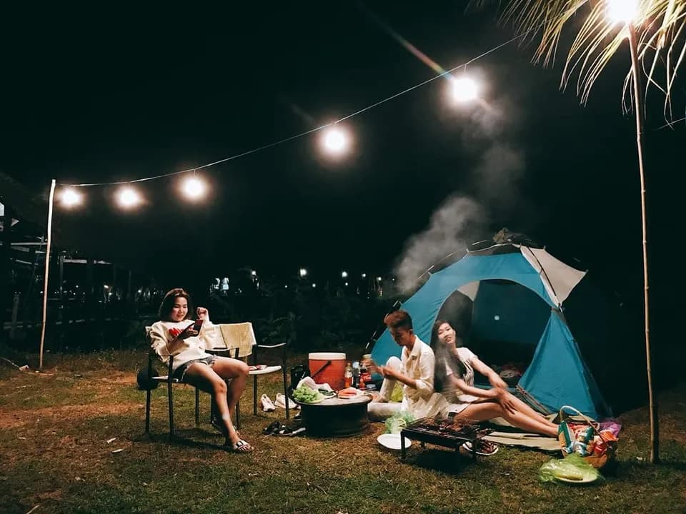 Nhóm bạn thư giãn quanh lều xanh và dây đèn trong đêm